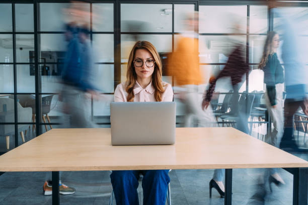 businesswoman working on laptop in a busy office. - concentratie fotos stockfoto's en -beelden