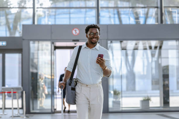 istock Smiling traveler using phone while walking through modern public transportation terminal 2204933797