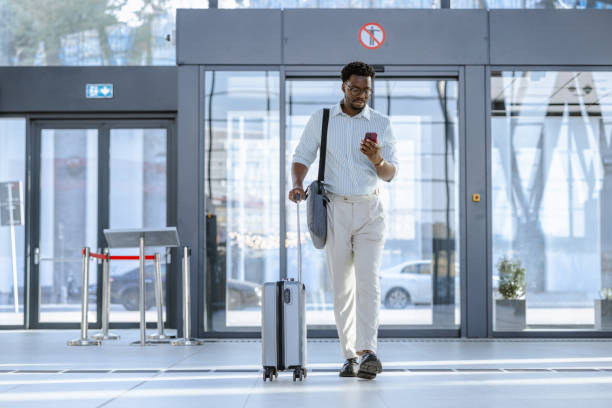 istock Smiling traveler pulling suitcase and holding a smartphone at modern transportation terminal 2204933926
