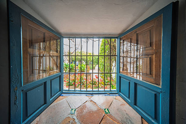 Open blue windows offer a glimpse into a vibrant courtyard full of colorful flowers in the historic Palace of Viana.