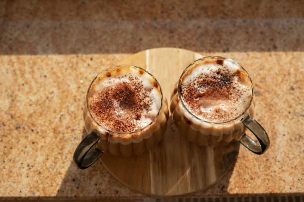 istock two frothy cappuccino mugs dusted with cocoa powder sit under warm sunlight on a textured wooden surface, creating a cozy and inviting atmosphere for coffee lovers. delight, wakeup, comfort, dining 2204943848
