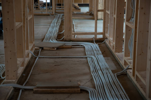 Interior view of a house under construction, featuring wooden framing, concrete floors, and organized ventilation or electrical conduits in early stages.
