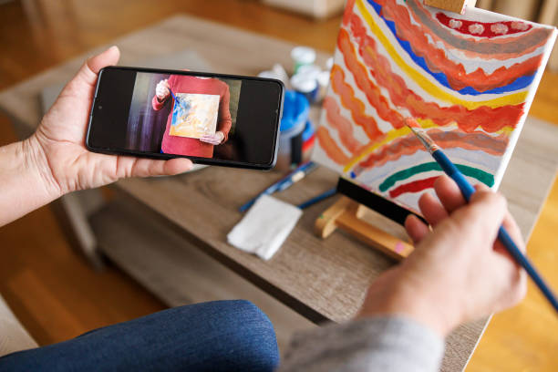 istock Woman taking online painting class watching tutorial using smart phone and painting on canvas 2204950965