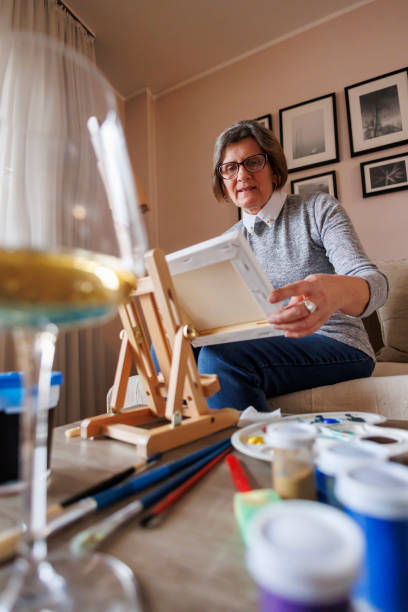 istock Senior woman adjusting easel and placing canvas while taking online painting class 2204951387