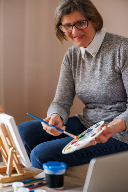 istock Senior woman having fun mixing colors while taking online painting class 2204951861