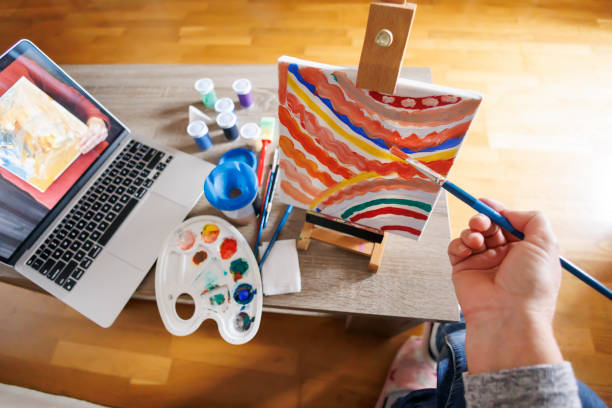 High angle view detail of senior Caucasian woman painting on canvas while taking online painting lesson at home