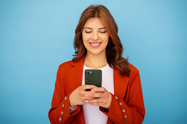 istock Young businesswoman smiling and using mobile phone on blue background 2204957694