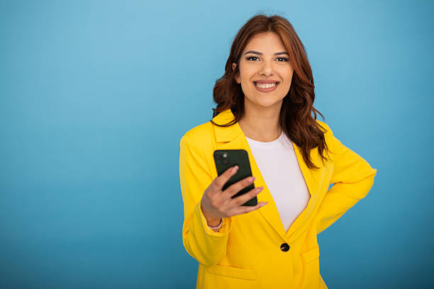 istock Young businesswoman smiling and using her smartphone on blue background 2204958961