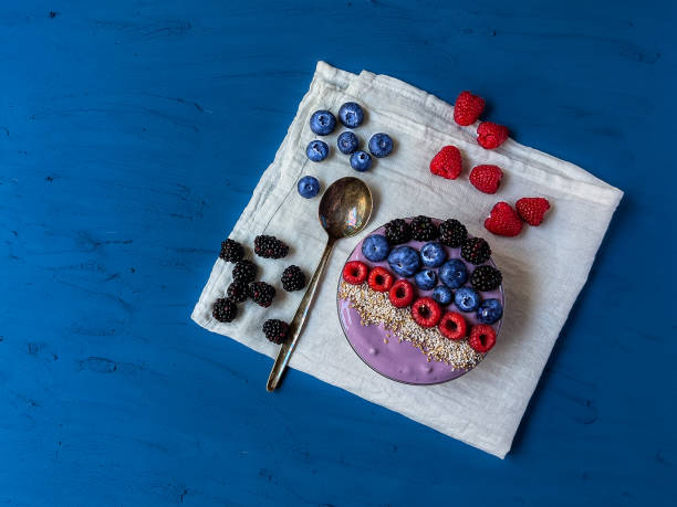 Skyr and various sorts of berries in glass bowl on dark blue table