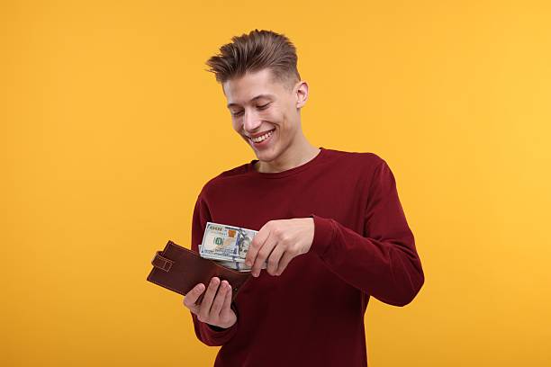 istock Happy man putting money into wallet on yellow background 2204965989