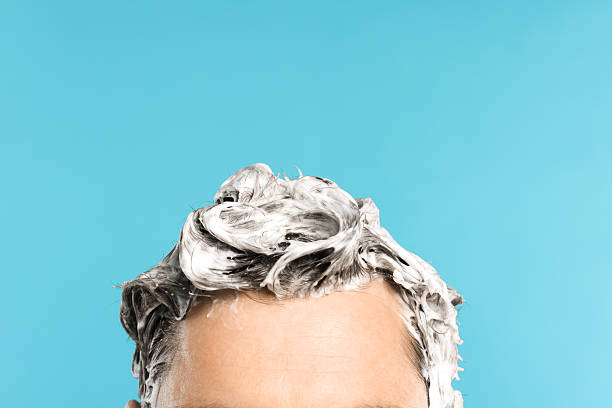 Man with shampoo foam on his head against light blue background, closeup. Space for text