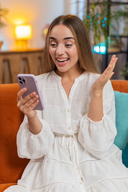 istock Excited woman sitting on sofa using smartphone typing browsing reading good news celebrating victory 2204972686