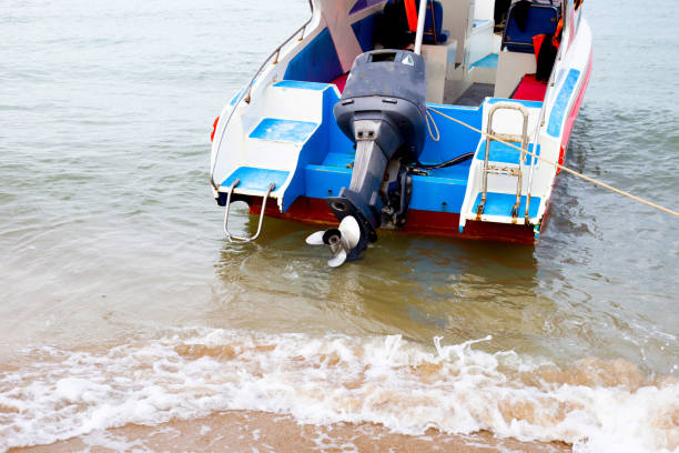 A brightly colored speedboat is partially beached on a sandy shore, with its outboard motor tilted up out of the water
