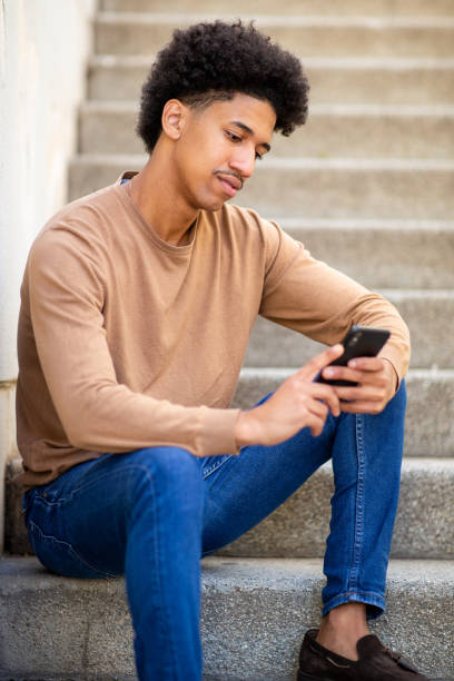 istock young hispanic man sitting on stairs with smart phone 2204976325