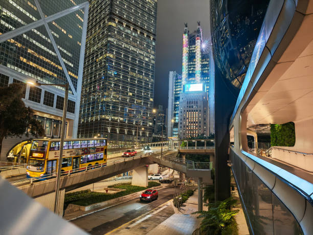 Hong Kong, China - March 12, 2025 : Night cityscape featuring illuminated skyscrapers and busy streets with a double-decker bus and cars. An elevated walkway adds another layer to the urban scene.