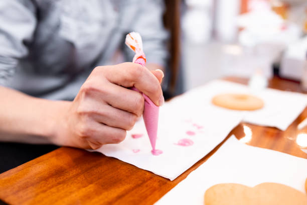 istock Adult female decorating cookies with pink icing using a piping bag in a kitchen setting 2204988838