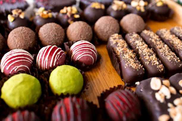 istock Assorted gourmet chocolate truffles and bars with nut toppings on wooden table 2204988890