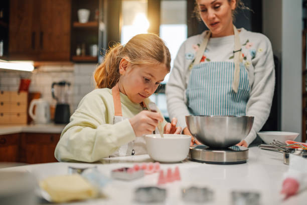 istock Daughter mixing ingredients while mother supervises in kitchen 2204991229