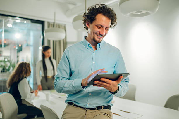 istock Businessman using digital tablet in modern office with colleagues working in the background 2204991634