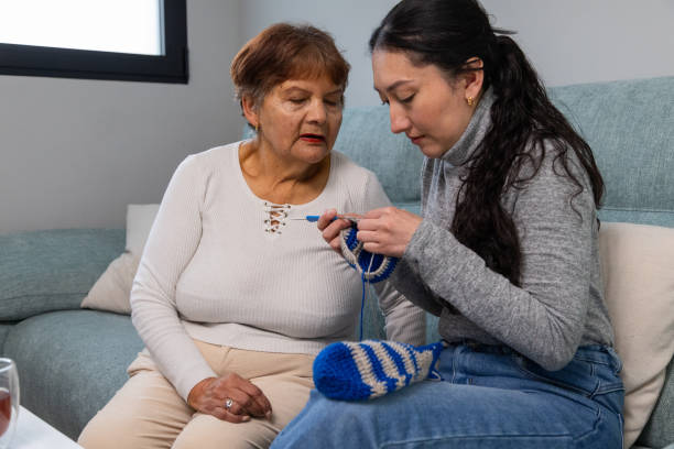 istock Nurse assisting elderly woman knitting on sofa at home 2204992532