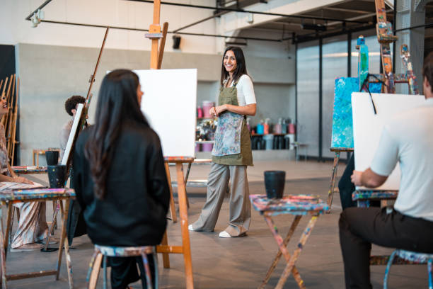 istock Young Middle Eastern Art Instructor Teaching Techniques to Students at Painting Easels in Studio Class 2204993721