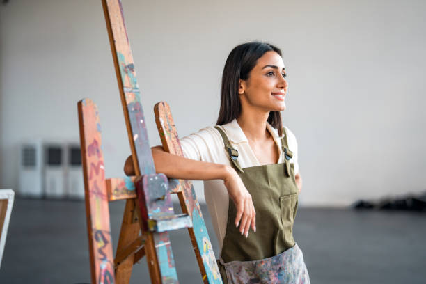 istock Young Middle Eastern Female Painter in Bright Studio Wearing Olive Green Apron 2204993872