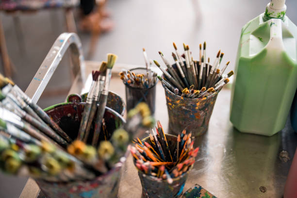 istock Colorful Art Brushes in Paint-Stained Containers on Studio Table 2204993894