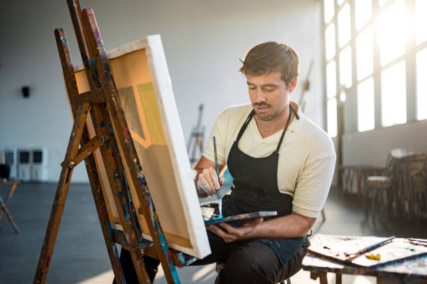 istock Focused Mid Adult Male Painter Creating Artwork in Sunlit Studio 2204993919