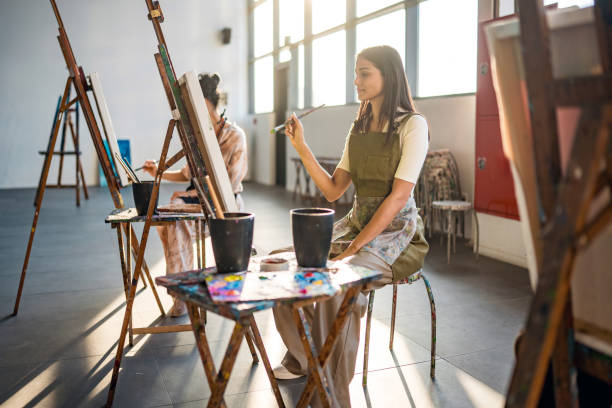 Middle Eastern Women Painting in Bright Art Studio Wearing Aprons and Focused on Creative Expression