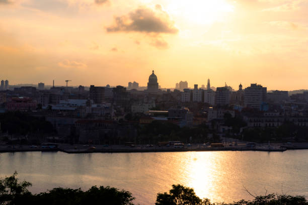 A stunning view of the Havana skyline at sunset, featuring the silhouette of El Capitolio and city buildings reflecting golden light over the bay.
