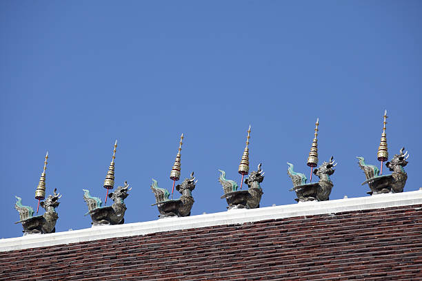 This image features ornate decorations atop a temple roof, showcasing mythical creatures and elegantly crafted spires against a clear blue sky. Perfect for cultural themes.