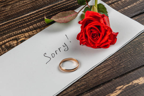 istock Broken engagement message with a ring and red rose on a wooden table 2205004617
