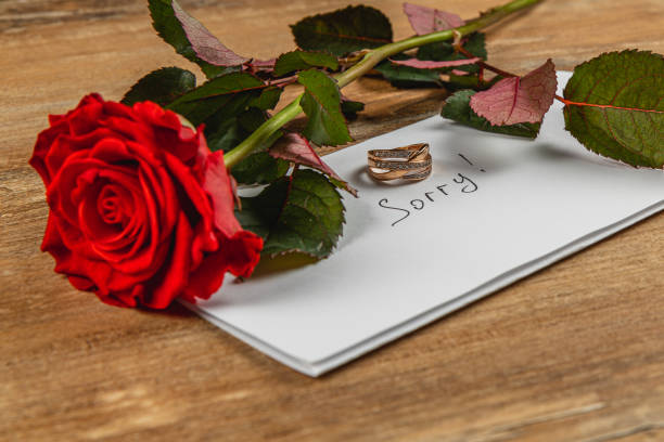 istock Broken engagement note with a rose and wedding rings on a wooden table 2205005720