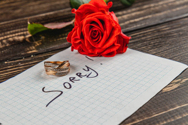istock Broken engagement with rings and a red rose on a wooden table 2205005753