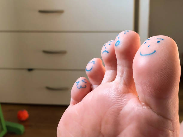 A close-up of a foot with faces drawn on each toe, expressing different emotions. A creative and fun concept blending humor and body art in a casual indoor setting.