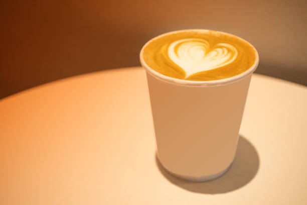 Hot coffee latte art in paper cup on white table with warm tone