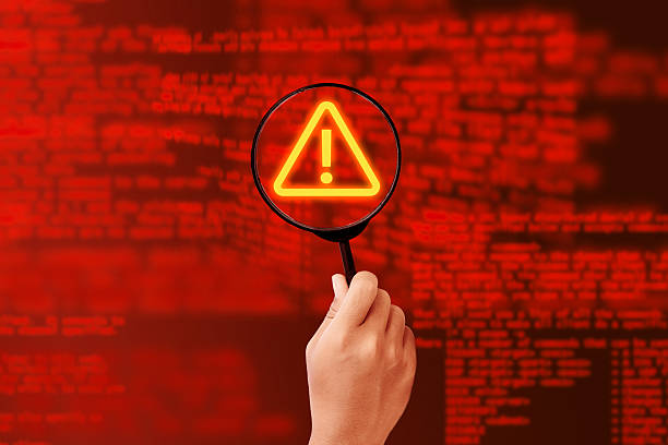 istock A person is holding a magnifying glass over a computer screen with a red background and a red triangle with an exclamation point 2205016670