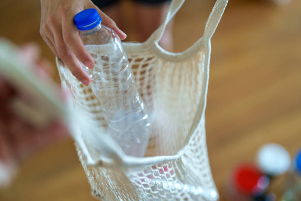 A person places a used plastic bottle into a reusable mesh bag, promoting an eco-friendly and sustainable lifestyle with a focus on recycling and reducing waste.