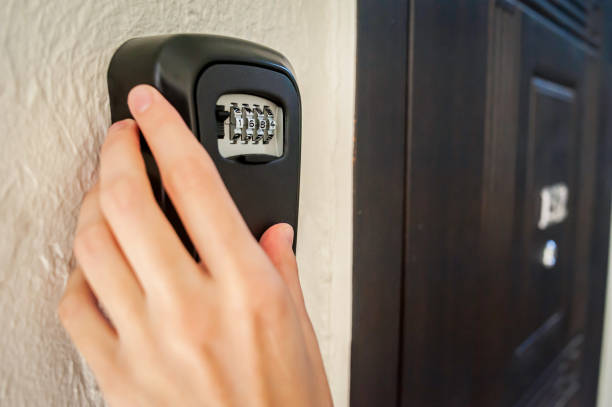 A hand is positioned by a combination lock mounted on a wall, indicating an attempt to secure personal items in a storage box. The setting appears to be at home.