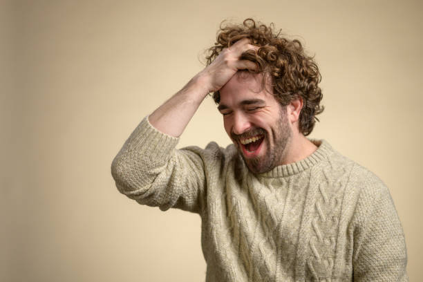 istock Laughing Young Man in Cream Cable Knit Sweater Against Beige Background 2205028263