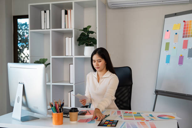 istock Concentrated woman designer selecting color palettes while analyzing project documents in her office 2205034031