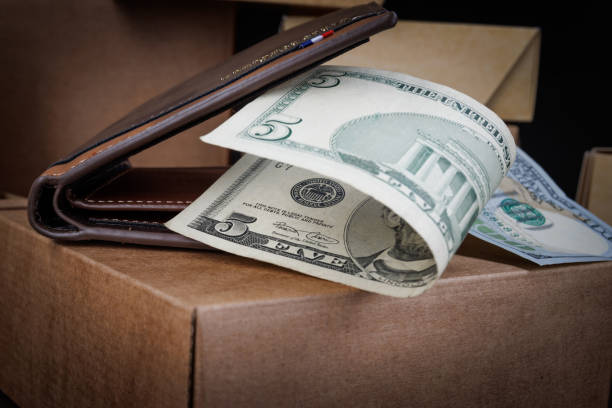 A leather wallet with dollar bills lies on paper boxes.