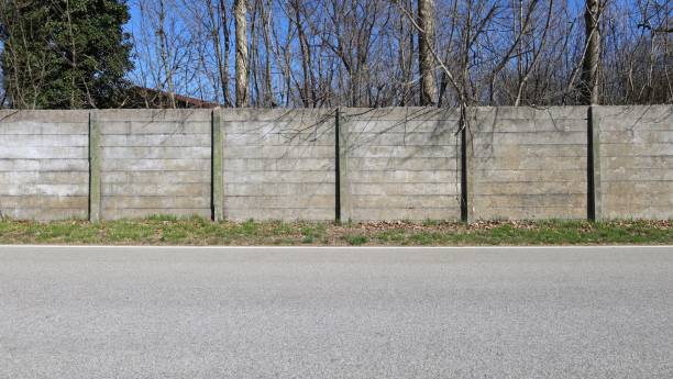 istock Grunge concrete precast compound wall at the road side with bare trees on behind and road in front 2205036969