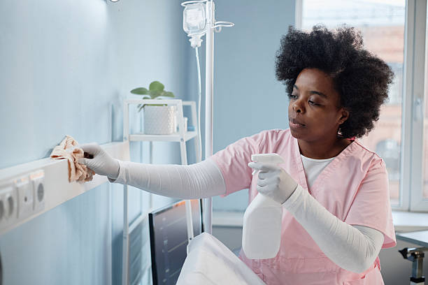 Medical professional diligently cleaning hospital room, ensuring hygiene and safety. African American woman focused on task, displaying dedication and care in healthcare environment