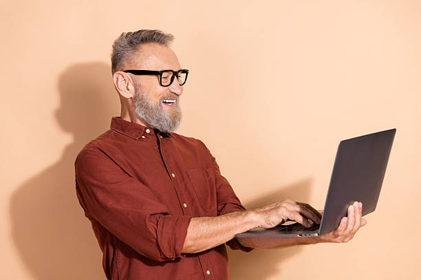 istock Mature man with stylish beard working on laptop against beige background, representing business, technology, and professional lifestyle 2205039200