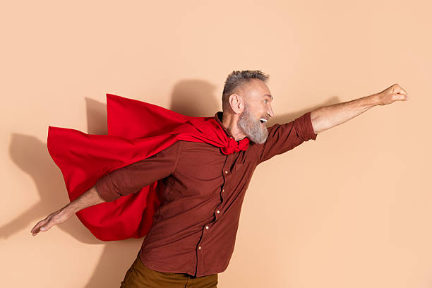 istock Senior man in red cape posing as a superhero on beige background, mid-action, symbolizing energy, confidence 2205039272