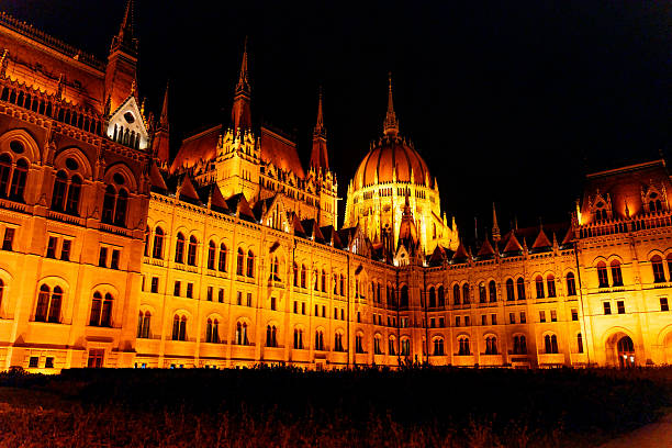 Budapest, Hungary - November 24, 2024: Panoramic view of the Hungarian Parliament Building lit up in orange at night, showcasing its stunning architecture and tall spires.