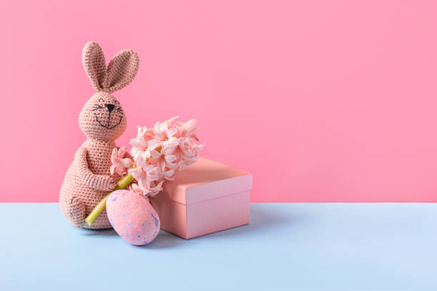 Gift box, knitted toy pink bunny with Easter egg and bouquet of spring flower hyacinth on blue table and purple background. Concept of Easter