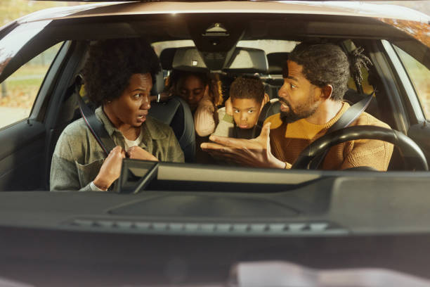 Displeased African American parents arguing while going on a trip with their small kids by car. The view is through windshield.