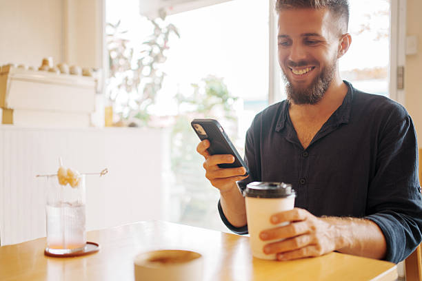 istock A Smiling Man Delightfully Enjoying His Coffee Beverage and Using His Phone in a Cozy Cafe 2205042338